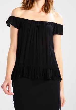 Femme portant un haut noir épaules dénudées avec un ourlet et des manches à volants, associé à une jupe noire ajustée.