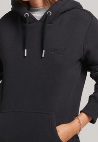Felpa nera con cappuccio realizzata in morbido tessuto, dotata di tasca frontale, cappuccio con cordino e dettaglio del logo sul petto in un design tonale sobrio.
