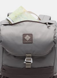 Light gray Columbia backpack with top flap, metal buckle, and a folded topographic map partially visible in the zippered compartment.