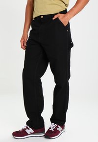 Zwarte denim broek met een recht model, voorzien van zijzakken en een subtiele stiksel detail. Gekocht met bordeauxrode sneakers en een beige shirt.