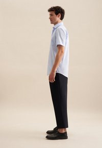 Camicetta azzurra a maniche corte con taschino sul petto, abbinata a pantaloni scuri e scarpe nere. Design semplice, texture liscia, vestibilità casual.