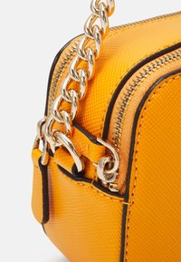 Bolso de cuero texturizado amarillo con una cadena dorada y detalles de cremallera. Presenta acentos negros y una forma rectangular compacta.
