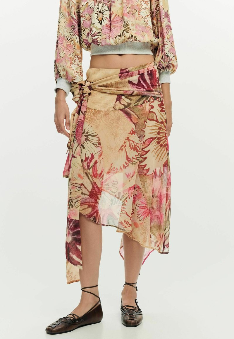 Femme portant un haut floral dévoilant le ventre et une jupe portefeuille fleurie asymétrique, associée à des ballerines noires à lacets.