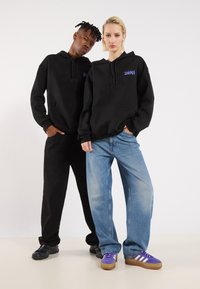Black hoodies with front pockets, paired with loose-fit blue jeans. Sneakers: black and purple with white stripes. Simple, casual attire.