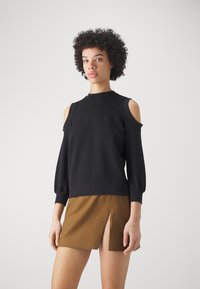 Sudadera negra de hombros al descubierto con mangas largas y abullonadas, y dobladillo acanalado, combinada con una falda mini marrón con una abertura frontal.