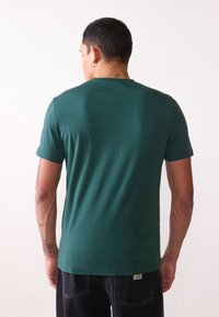 Zelené tričko s krátkým rukávem a kulatým výstřihem vyrobené z měkké bavlny, s hladkou texturou a minimalistickým designem bez vzorů nebo akcentů.
