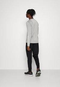 Camisa gris de manga larga con corte ajustado, combinada con pantalones negros de corte holgado y zapatillas deportivas negras con suelas texturizadas y detalles en blanco.