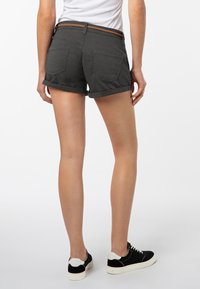 Donkergrijze shorts met opgerolde omslag, voorzien van twee achterzakken en een bruine gevlochten riem. Gecombineerd met zwarte sneakers.