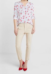 Blus med blommönster och ränder, v-ringning och uppvikta ärmar, kombinerad med beiga figurnära byxor och röda klackskor.