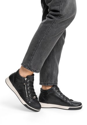 Person wearing black textured high-top sneakers with white soles and black laces, paired with dark grey jeans.