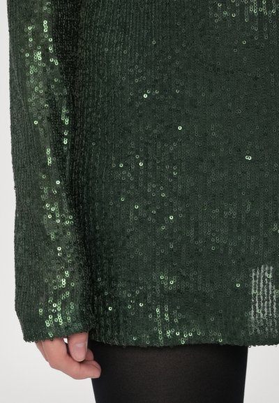 Zöld, flitteres felső texturált kötött anyagból; hosszú ujjakkal és bő szabással; fényes flitterek borítják az egész felületet.