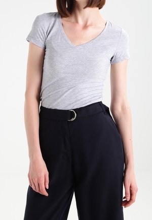 Szara koszulka z krótkim rękawem i dekoltem w serek w połączeniu z granatowymi, wysokim stanem spodniami z okrągłą klamrą paska, prezentująca gładką fakturę tkaniny.
