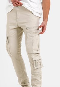 Beige cargobroek met meerdere zakken, ritssluitingen en gestikte details. De stof heeft een fijne textuur en een slim fit ontwerp.