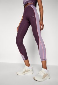 Lila és levendula színű leggings pink részletekkel, magas derékkal, légáteresztő anyagból, szoros illeszkedéssel, fehér sportcipővel párosítva.