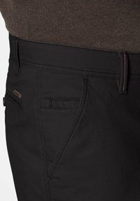 Schwarze Hosen aus strukturiertem Material, mit Reißverschluss, Akzentnähten und einem kleinen Logodetail am Bund.