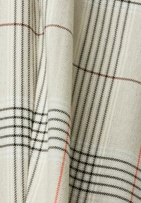 Tissu crème avec un motif écossais noir, marron et orange comprenant des lignes verticales et horizontales qui se croisent.