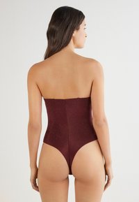 Bordowy jednoczęściowy kostium kąpielowy bez ramiączek z wysokim krojem nogawki i teksturowanym, lśniącym materiałem, z dopasowanym topem i minimalnym zakryciem pleców.