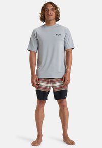 Camiseta de surf de manga corta gris con logo; bañador a rayas en beige, rojo y azul marino; tejido ligero y de secado rápido.