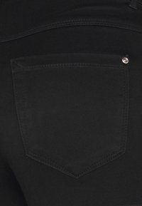 Pantalones de mezclilla negros con un único bolsillo trasero de forma puntiaguda, detalles en remaches plateados y costuras contrastantes.