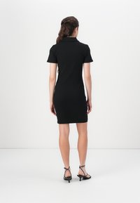 Black polo dress with short sleeves and a fitted design, featuring ribbed texture and a knee-length hem. Accompanied by strappy black heels.