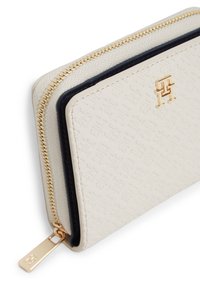 Πορτοφόλι σε υφή κρέμας με χρυσό φερμουάρ και λογότυπο, διακοσμημένο με σκούρο μπλε περιθώριο. Κομψός σχεδιασμός με απαλό εξωτερικό και χρυσά μεταλλικά στοιχεία.