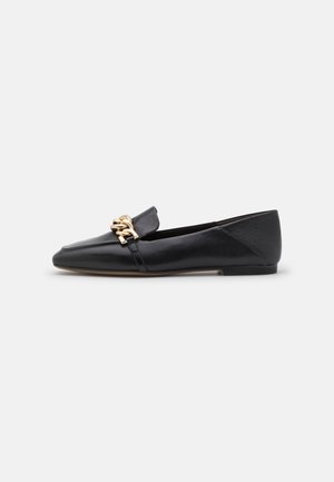 Mocassin plat en cuir noir avec bout pointu et détail chaîne dorée sur le dessus, présenté de profil sur fond blanc.