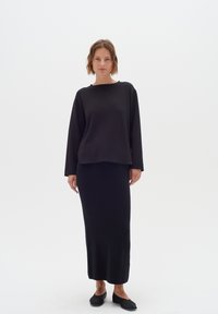 Top nero a maniche lunghe con scollatura a girocollo abbinato a una gonna maxi nera aderente. Entrambi i capi presentano una texture liscia e un design minimalista.