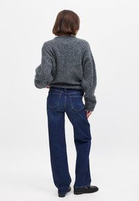 Hallikas karvane sviiter, millel on õhupallikujulised varrukad, sobitatud tumedate siniste laiadest pükstest. Riietusel on tekstureeritud kangas ja klassikalised teksariide detailid.