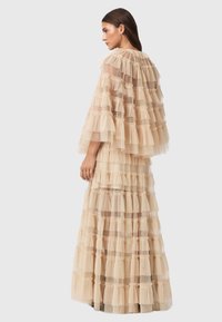 Γυμνό φόρεμα από τούλι με στρωματοποιημένες φουσκωτές, μακριές μανσέτες, και σχεδιασμό με επίπεδα. Μαλακή υφή με διαυγή και αδιαφάνεια τμήματα σε όλη την επιφάνεια.