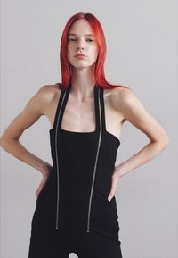 Black sleeveless jumpsuit with a square neck and thin, metallic-accented straps. Smooth texture with fitted design and minimal detailing.