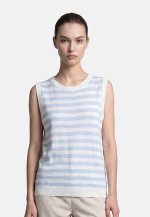 Giovane donna con capelli raccolti che indossa una canotta bianca senza maniche con strisce orizzontali azzurro chiaro e pantaloni beige su sfondo semplice.