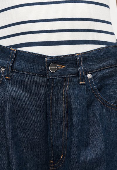 Dark blue denim jeans with orange stitching and metal button closure branded "DONDUP," paired with a white and navy striped top.