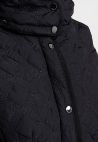 Přesně prošívaná černá péřová bunda s vysokým límcem, patentními knoflíky a texturovaným vzorem s procházejícími liniemi. Měkká, hladká látka.