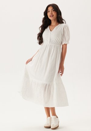 Robe blanche, longueur genoux, faite d'un tissu léger avec des motifs œillets, des manches courtes bouffantes, un décolleté en V et une jupe à volants.