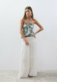 Top de halter floral en azul oscuro y blanco, con un frente anudado. Falda blanca fluida con volantes y una cinturilla fruncida. Textura de tela suave.