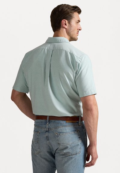 Kortermet skjorte i mintgrønn med krage og bakfylling, kombinert med lyseblå denimjeans og et brunt belte. Glatt stoffstruktur.
