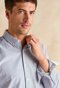 Niebiesko-biała, w pasiaki, koszula zapinana na guziki z kieszonką na piersi, wykonana z bawełny, z kołnierzykiem do złożenia i kontrastującym wnętrzem mankietów.