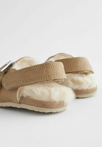 Béžové sandále so soft faux kožušinovým detailom, dvoma nastaviteľnými popruhmi a prešitým dizajnom. Sól je textúrovaný pre lepšiu priľnavosť.