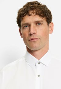 Weißes Hemd mit klassischem Kragen, aus glattem Stoff gefertigt, mit silbernen Knöpfen und einer dezenten Struktur auf der Oberfläche.