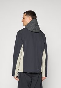 Men's jacket with a dark gray body, light gray side panels, and a textured gray hood. Features a relaxed fit and long sleeves.