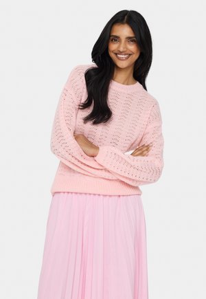 Light pink knitted sweater with a textured pattern, ribbed cuffs and hem. Worn over a pink pleated skirt, showcasing a relaxed fit.
