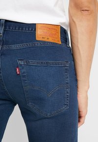 Mörkblå denimjeans med hög midja, med en läderpatch bak, klassiska sömmar och ett rött varumärkesmärke på bakfickan.