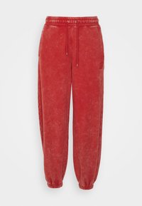 Rote Jogginghosen mit gebürsteter Textur, elastischem Bund mit verstellbarem Kordelzug und gerippten Bündchen. Verfügt über Seitentaschen und ein Logo-Patch.