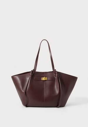 Mørkebrun læder tote taske med lange håndtag og en gylden rektangulær spænde foran, sat mod en enkel hvid baggrund.