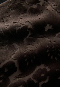 Dunkelbrauner Samtstoff mit einem erhabenen Blumenmuster. Die Textur ist weich und weist durchgängige, filigrane Details auf.