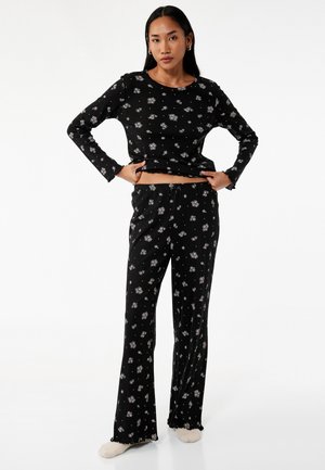 Sort pyjamakombination med blomsterprint, langærmet top og bukser med brede ben. Ribbet tekstur, cropped top, elastisk talje og flæset manchetter. Blødt stof.