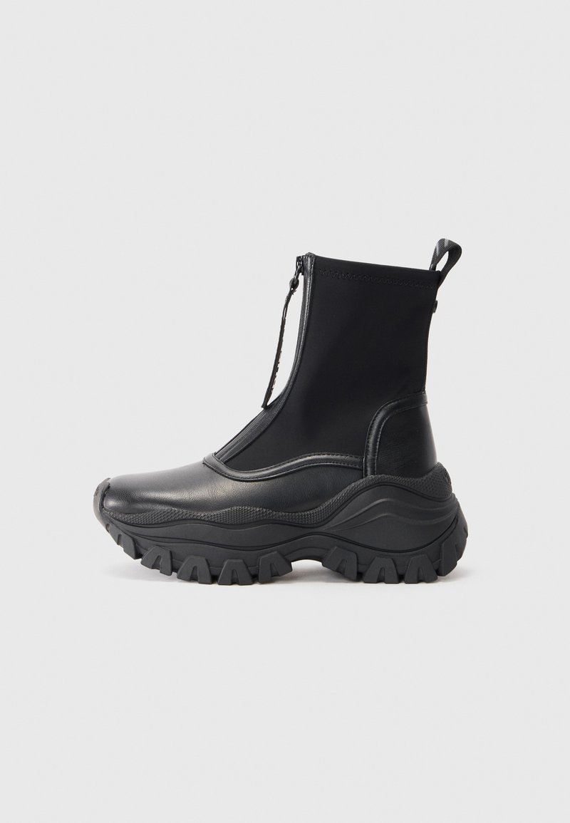 Bottines noires avec un extérieur en cuir lisse et une tige en tissu extensible. Dotées d'une semelle en caoutchouc épaisse et texturée et d'une fermeture éclair sur le côté.