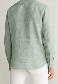 Camicia a maniche lunghe verde chiaro in lino tessutato, con orlo curvo, polsini a bottoni e un yoke posteriore con un piccolo dettaglio ad anello.