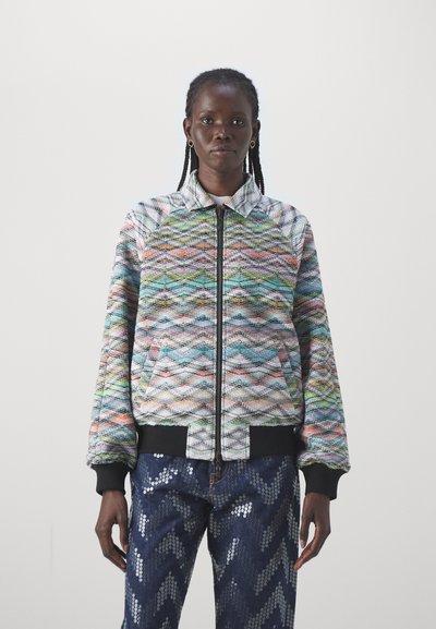 Veste bomber multicolore avec un motif en zigzag, tissu texturé, poignets et bas à côtes, associée à un pantalon bleu en zigzag avec sequins.