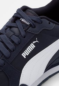 Merip navy dengan bagian atas kain tekstur dan aksen kulit putih. Logo PUMA ditampilkan dengan jelas di sisi dan lidah sepatu.